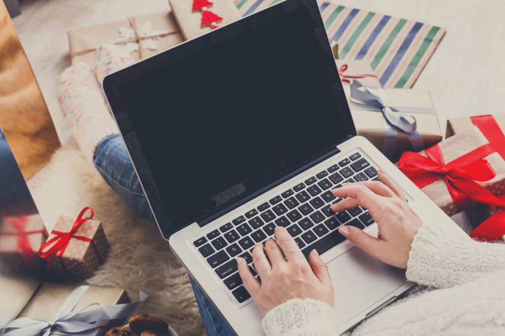 Christmas online shopping. Female buyer types order on laptop, copy space on screen. Woman buys presents prepare to xmas eve, among gift boxes and packages. Winter holidays sales
